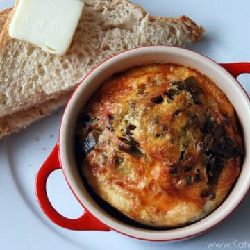 Red ramekin with a cheddar egg soufle on a white plate with two slices of toast with butter.