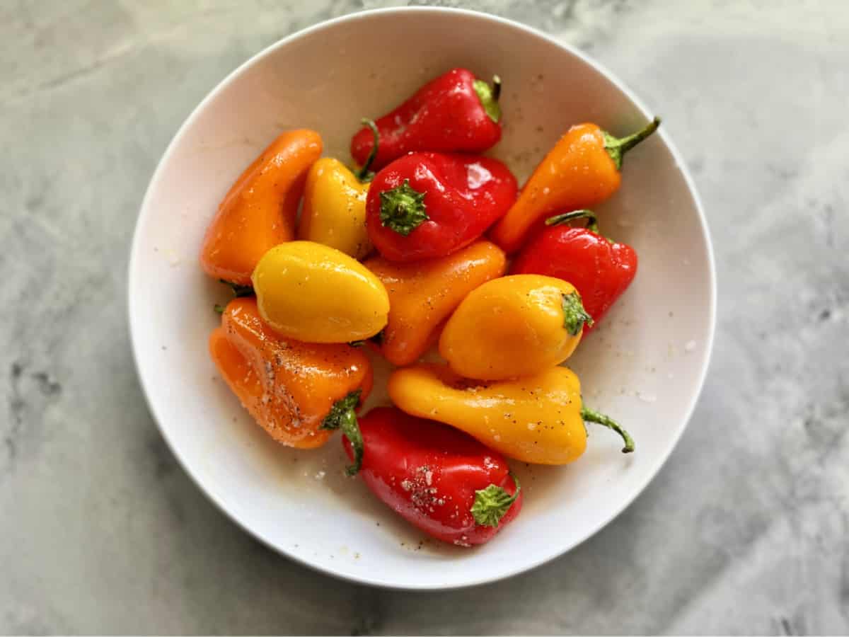 Top view of a white bowl on a marble countertop holding mini multi-color bell peppers.