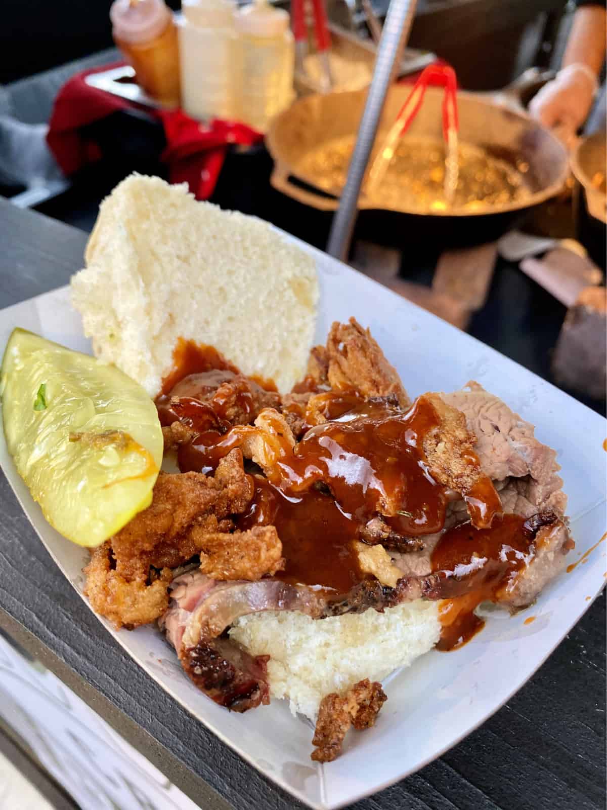 Paper tray holding brisket with barbecue sauce on a small bun with a pickle.