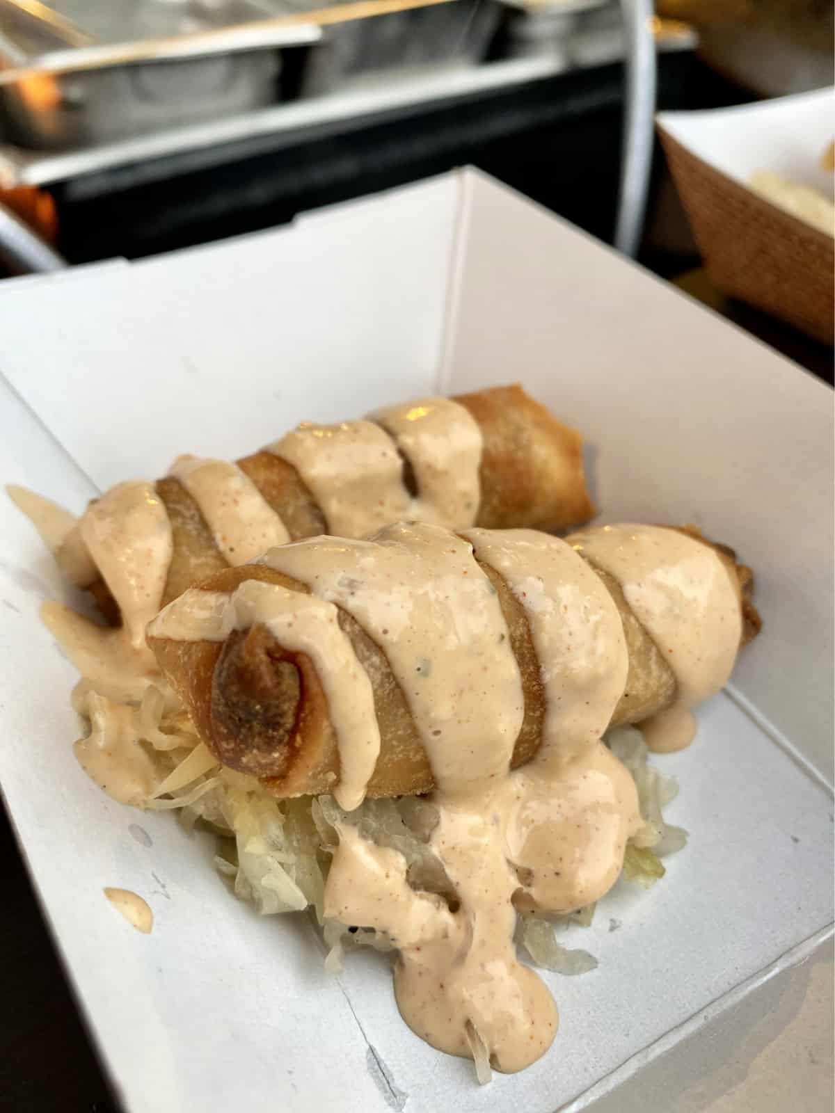 Two spring rolls on a bed of sauerkraut with thousand island dressing drizzled on top.