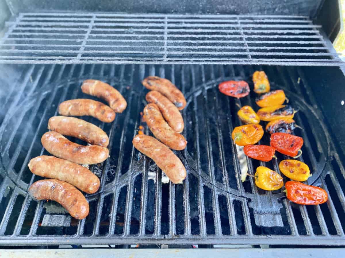 Italian sausage and charred multi-color mini bell peppers on a grill.