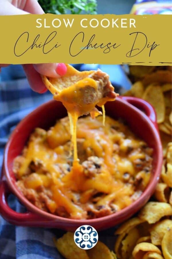 Female hand holding Frito chip with a cheesy dip pulling from a red dish.