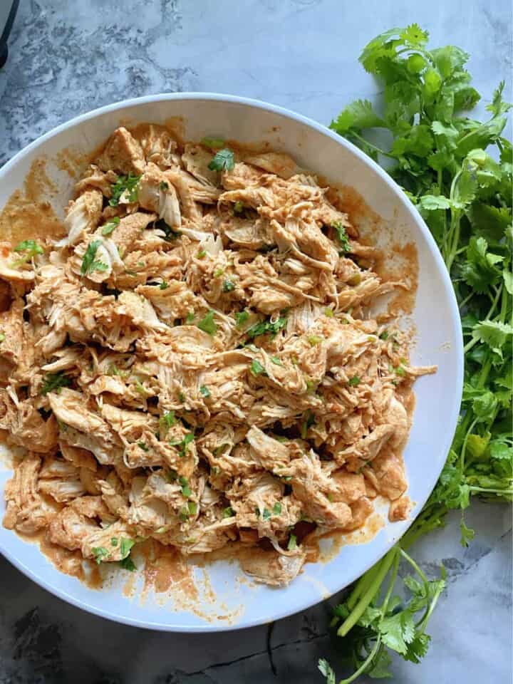 Top view of a white bowl filled with shredded chicken with cilantro on top and on the side.