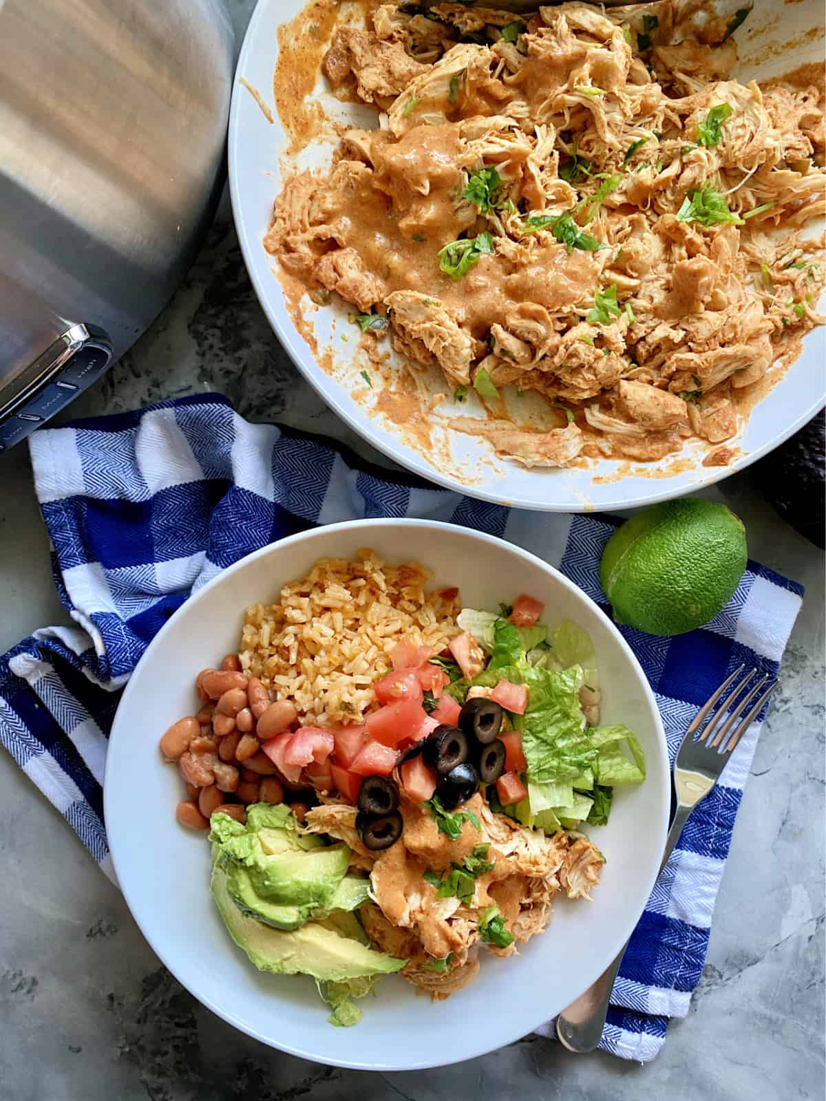 Top view of a white bowl filled with shredded chicken, rice, avocado, beans, lettuce, tomatoes, and olives.