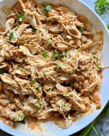 Top view of shredded chicken with cilantro in a white bowl.