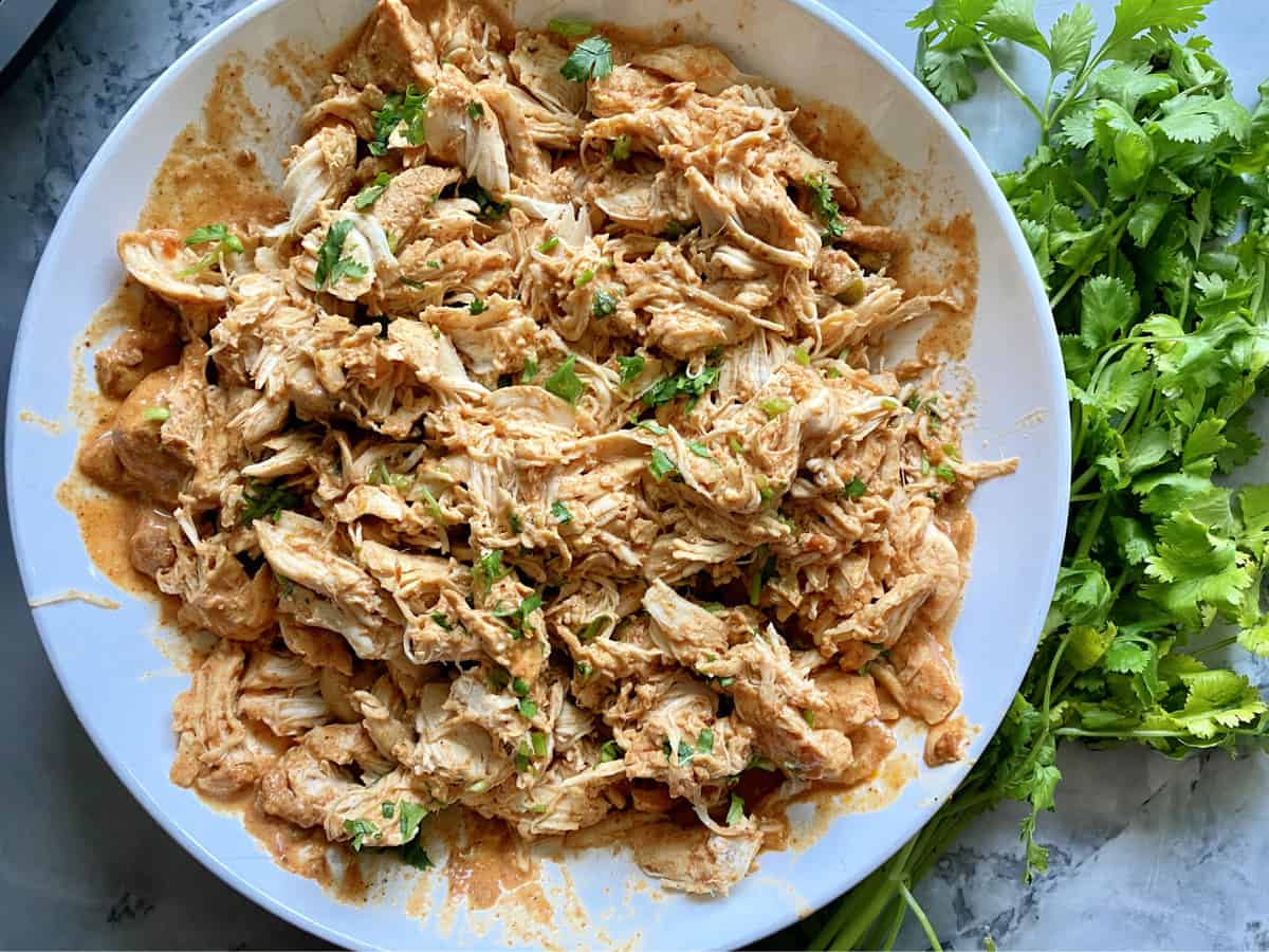 Top view of shredded chicken with cilantro in a white bowl.