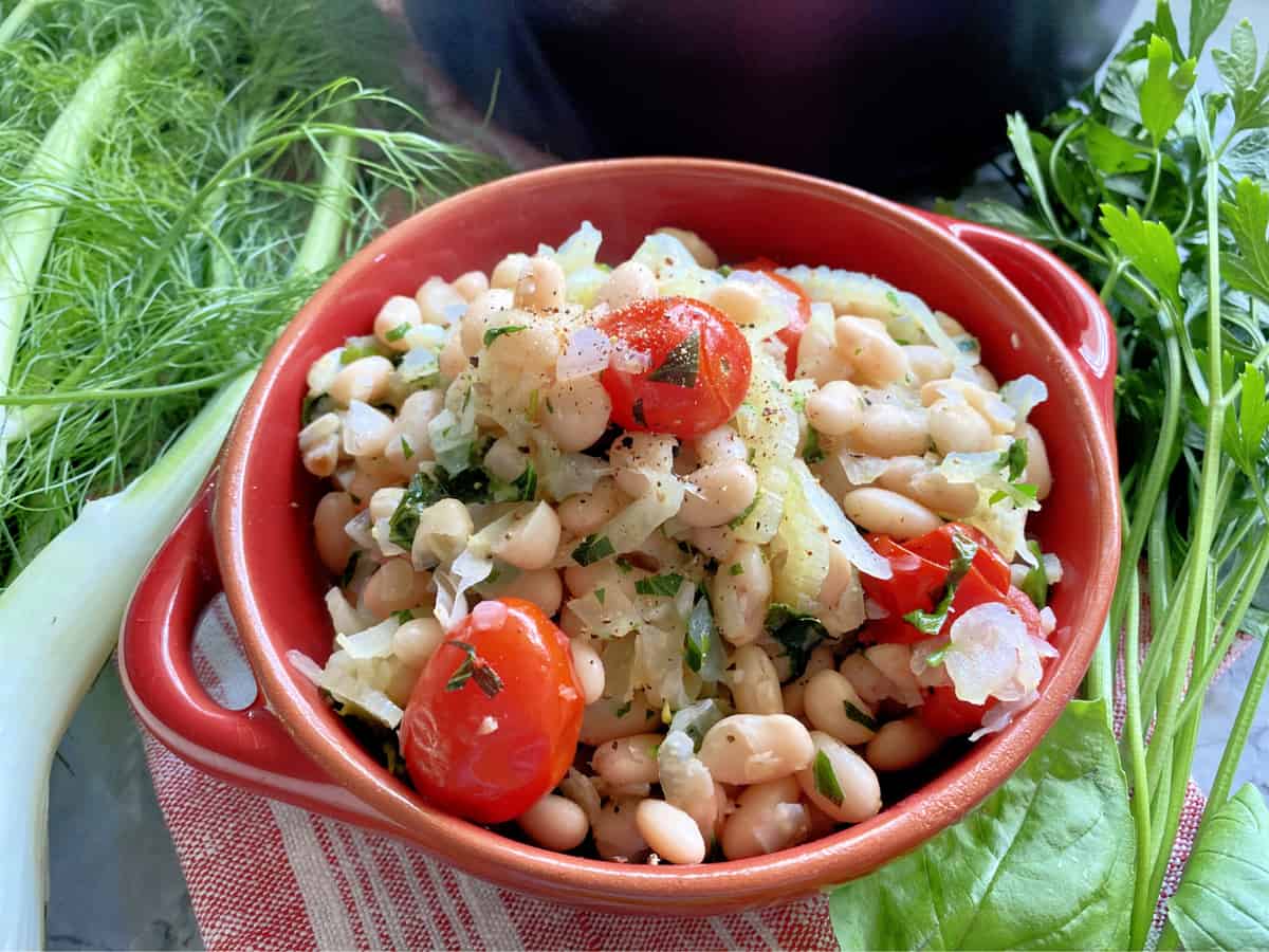 Red ceramic dish with white beans, caramelized fennel, grape tomatoes, and herbs. 