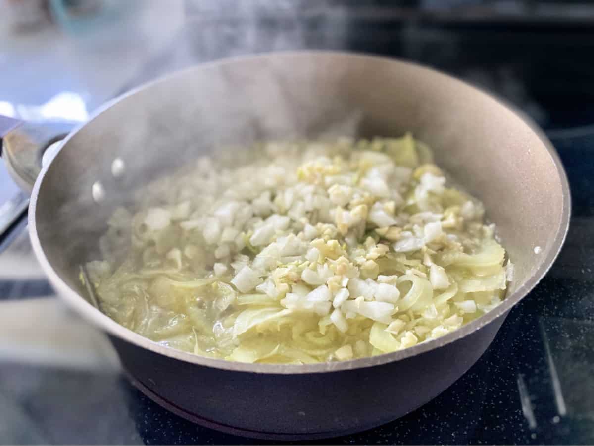 Brown skillet on stove with sauteed fennel, onions, and garlic. 