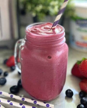 Glass mug filled with pink smoothie and purple and white paper straw