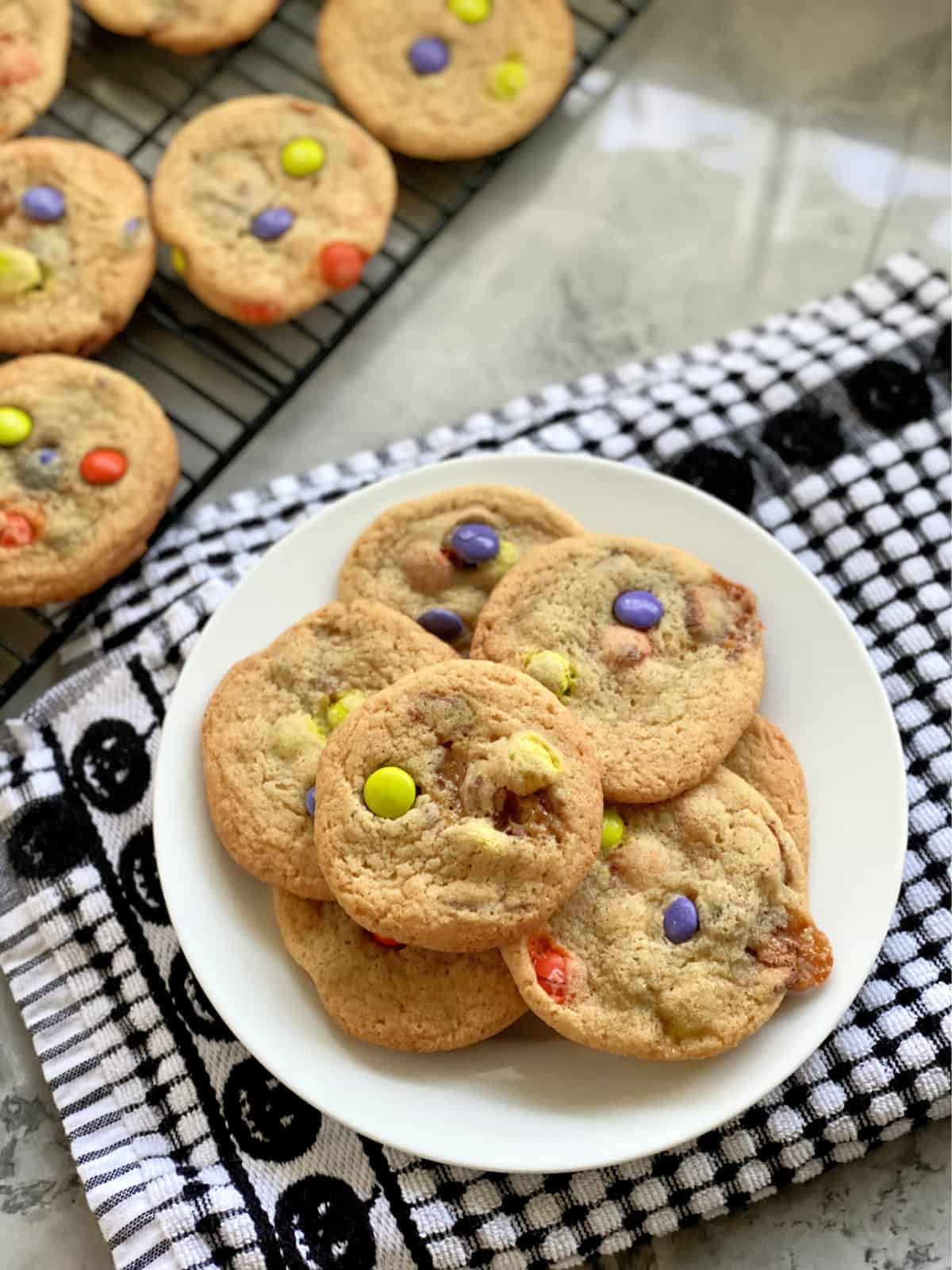 White plate filled with M&M cookies on a black and white dish cloth.