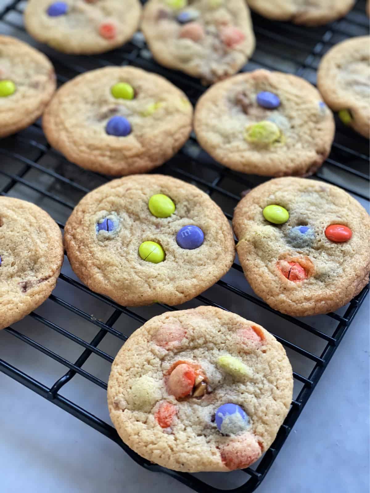 Black wire rack with M&M Cookies cooling on it.