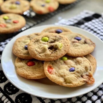Close up of a plate of cookies with candies in them and more cookies in the background.