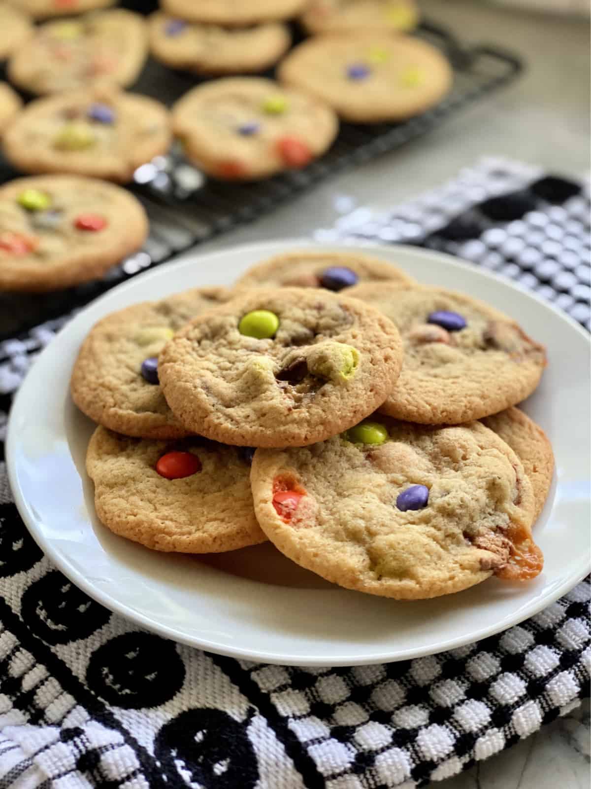 Close up of a plate of cookies with candies in them and more cookies in the background.