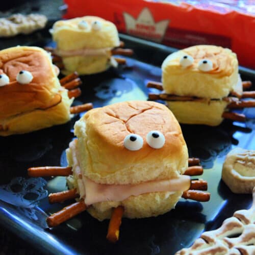 Four mini sandwiches that look like spiders with candy eyes and pretzels sticking out the sides.