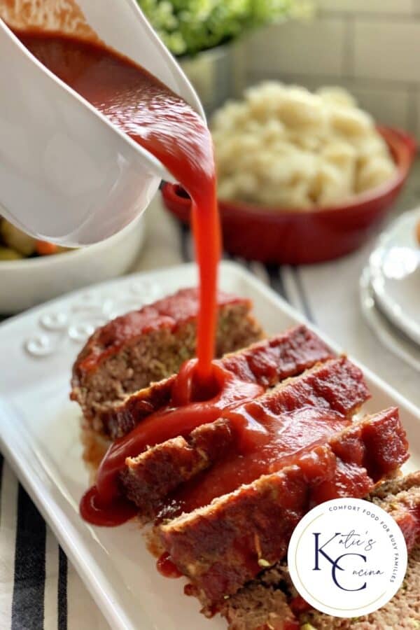 White gravy boat pouring red sauce on top of sliced meatloaf.