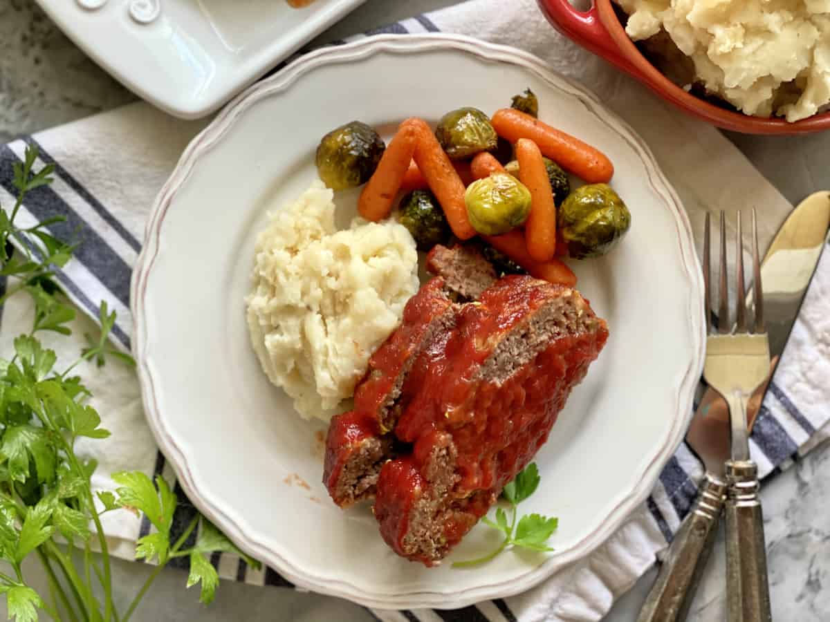 Top view of a plate of meatloaf, mashed potatoes, carrots, and Brussels sprouts.