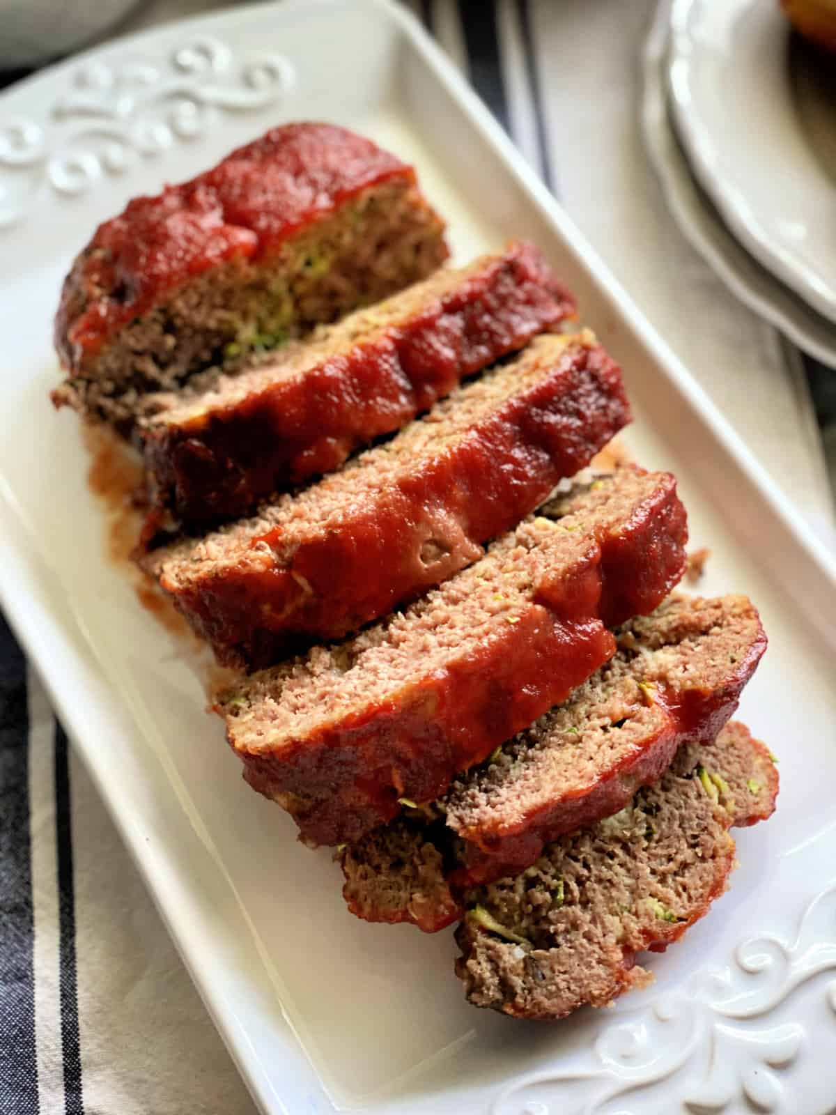 Top view of sliced meatloaf on a white platter with text on image for Pinterest.