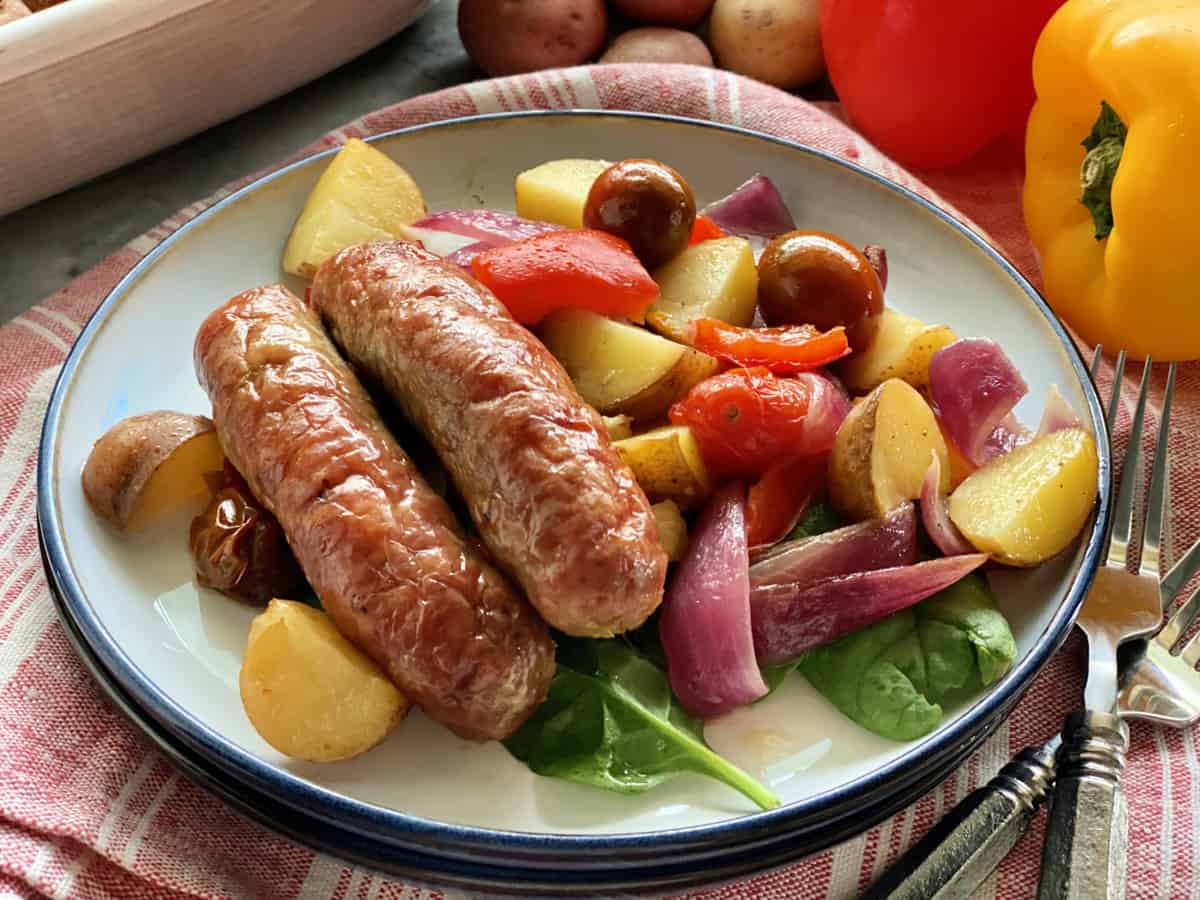 Two sausage links on a bed of spinach with potatoes and bell peppers.