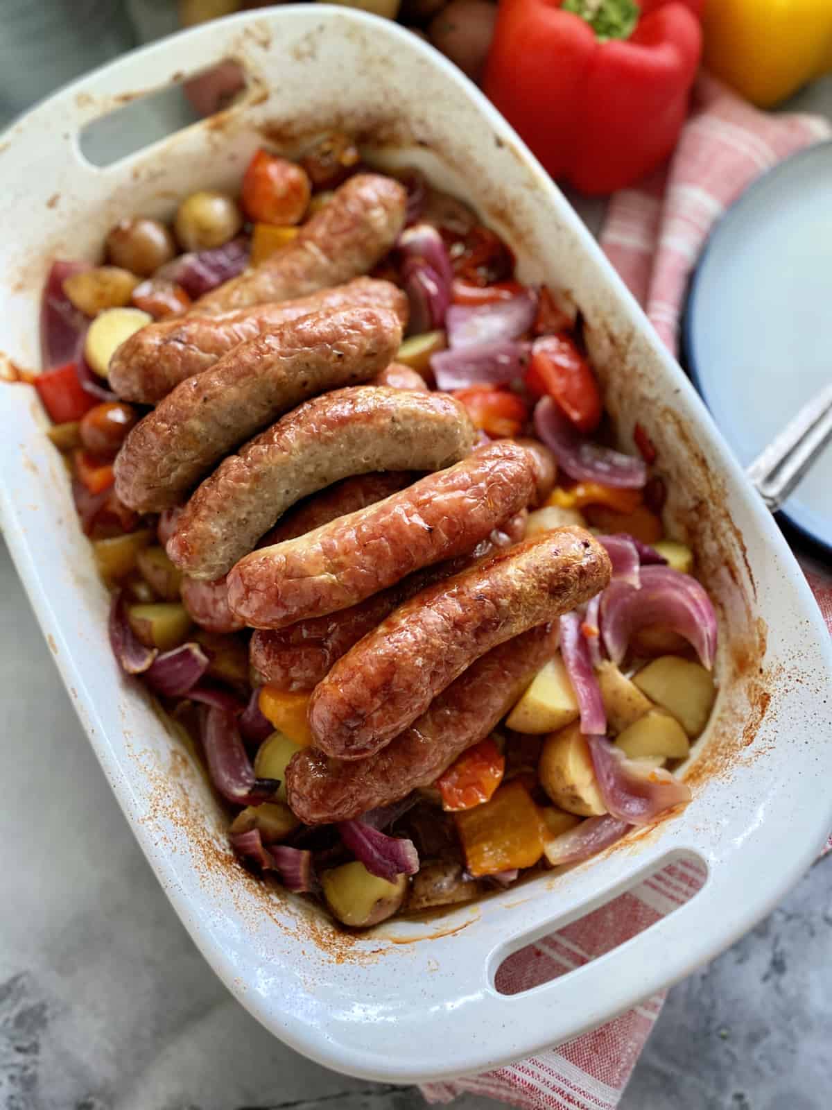 White casserole dish with roasted Italian sausage nestled on a bed of vegetables.