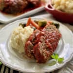 White plate with two slices of meatloaf with tomato sauce and mashed potatoes.