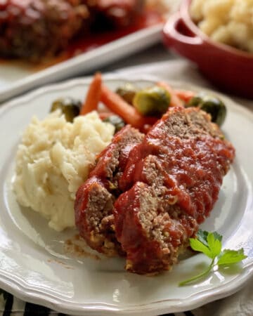 White plate with two slices of meatloaf with tomato sauce and mashed potatoes.