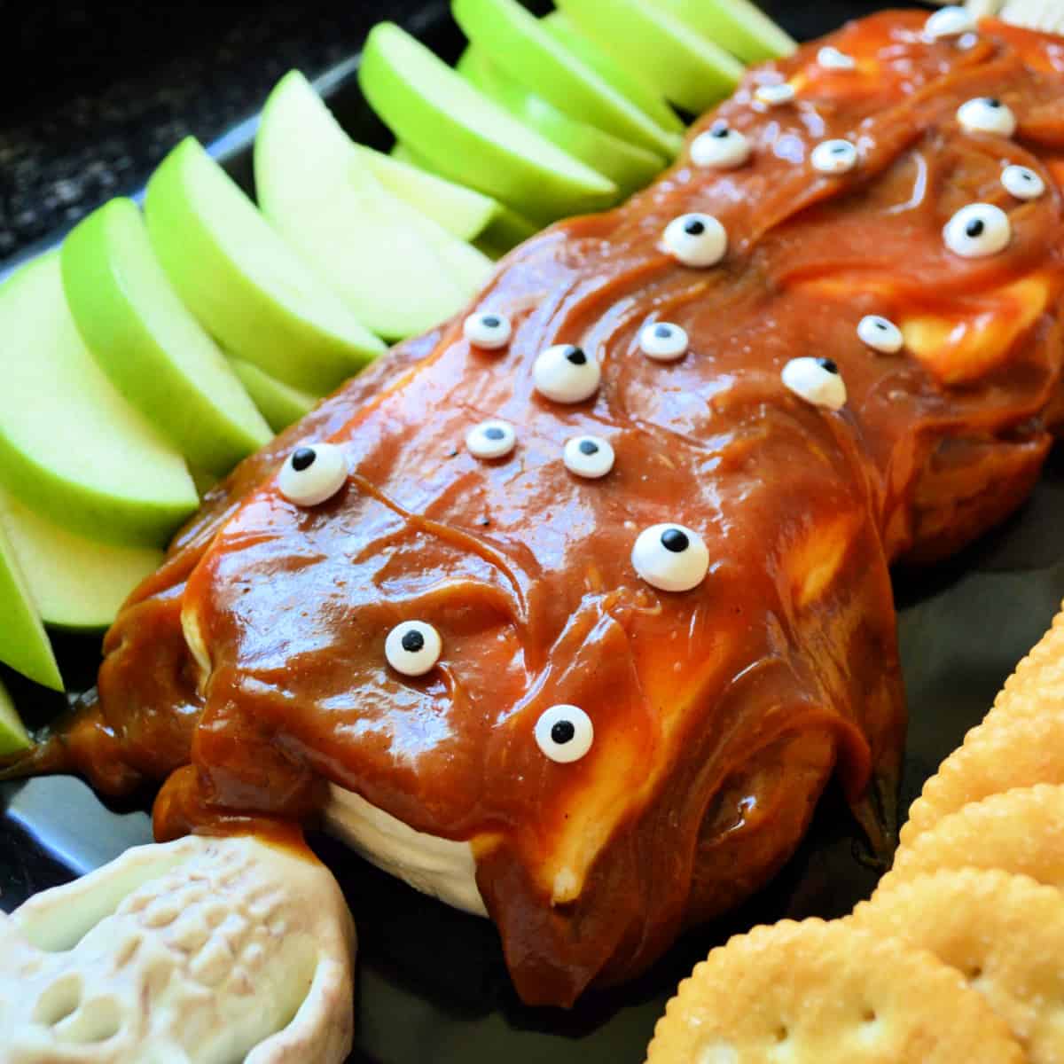 Cream cheese with carmel on top and eyeballs with apples and crackers on a tray.