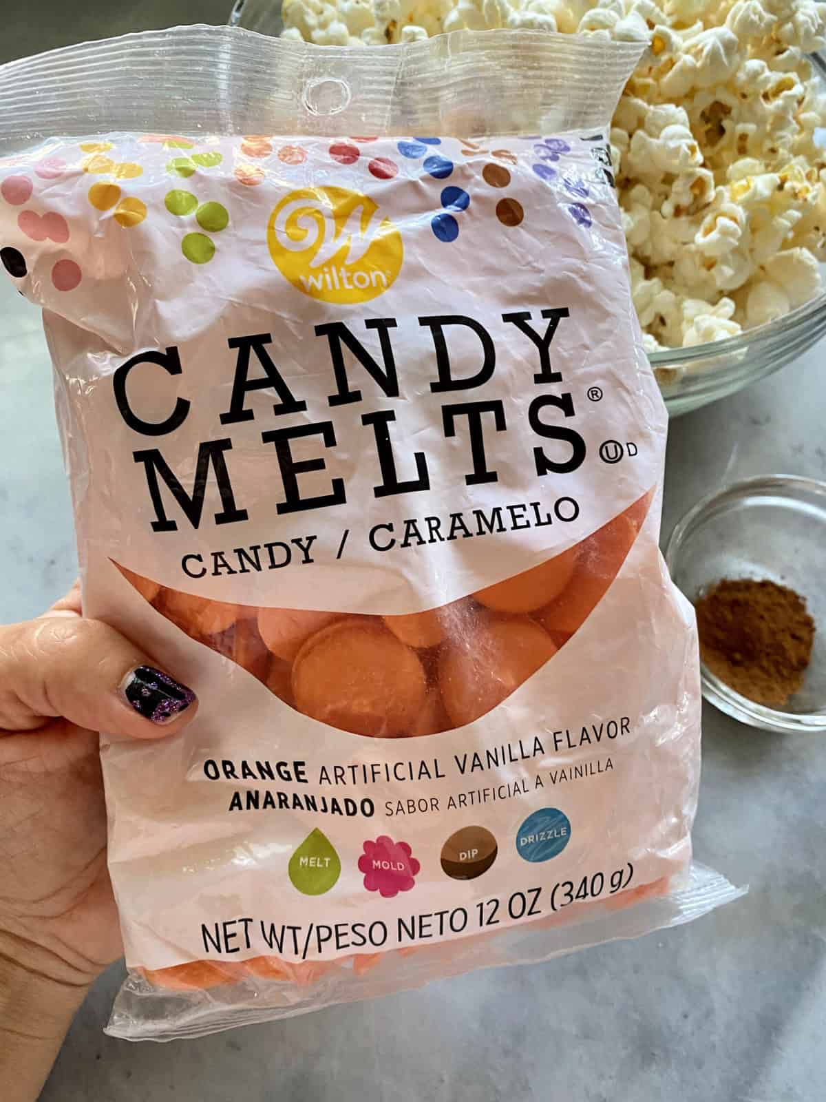 Female hand holding a bag of orange candy melts.