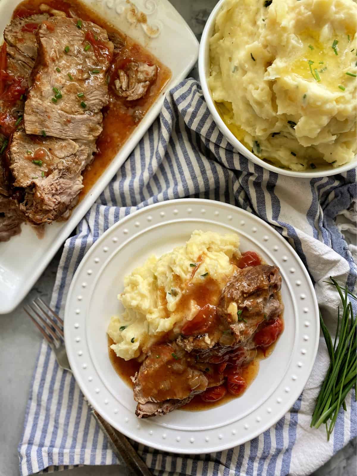 Top view of a white plate with mashed potatoes and sliced pork roast with gravy.