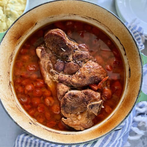 Top view of a cast iron green pot with a pork roast with tomatoes.