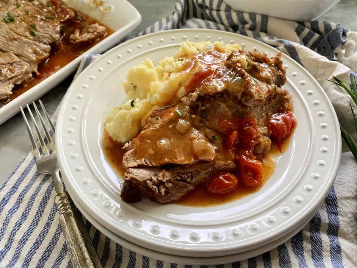 White plate with sliced pork roast with mashed potatoes and gravy.