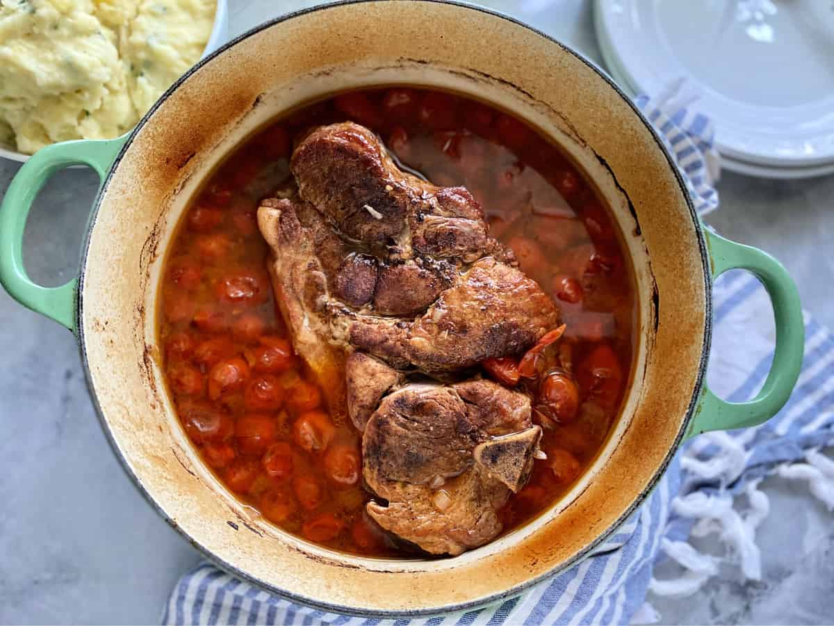 Top view of a cast iron green pot with a pork roast with tomatoes.