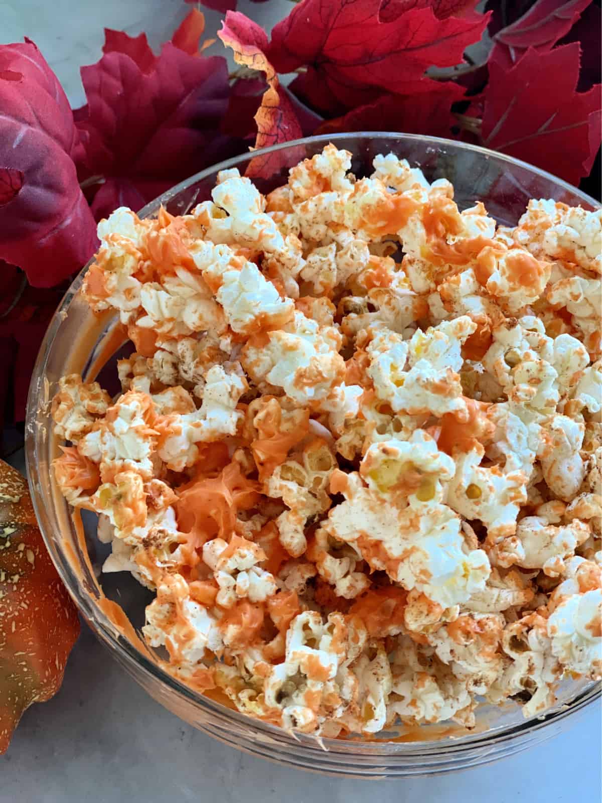 Top view of a bowl of orange chocolate popcorn with leaves.