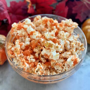 Glass bowl filled with orange popcorn with fall leaves in background.