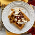 Top view of a white plate with two rectangular waffles with whipped cream and pecans.