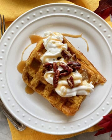Top view of a white plate with two rectangular waffles with whipped cream and pecans.