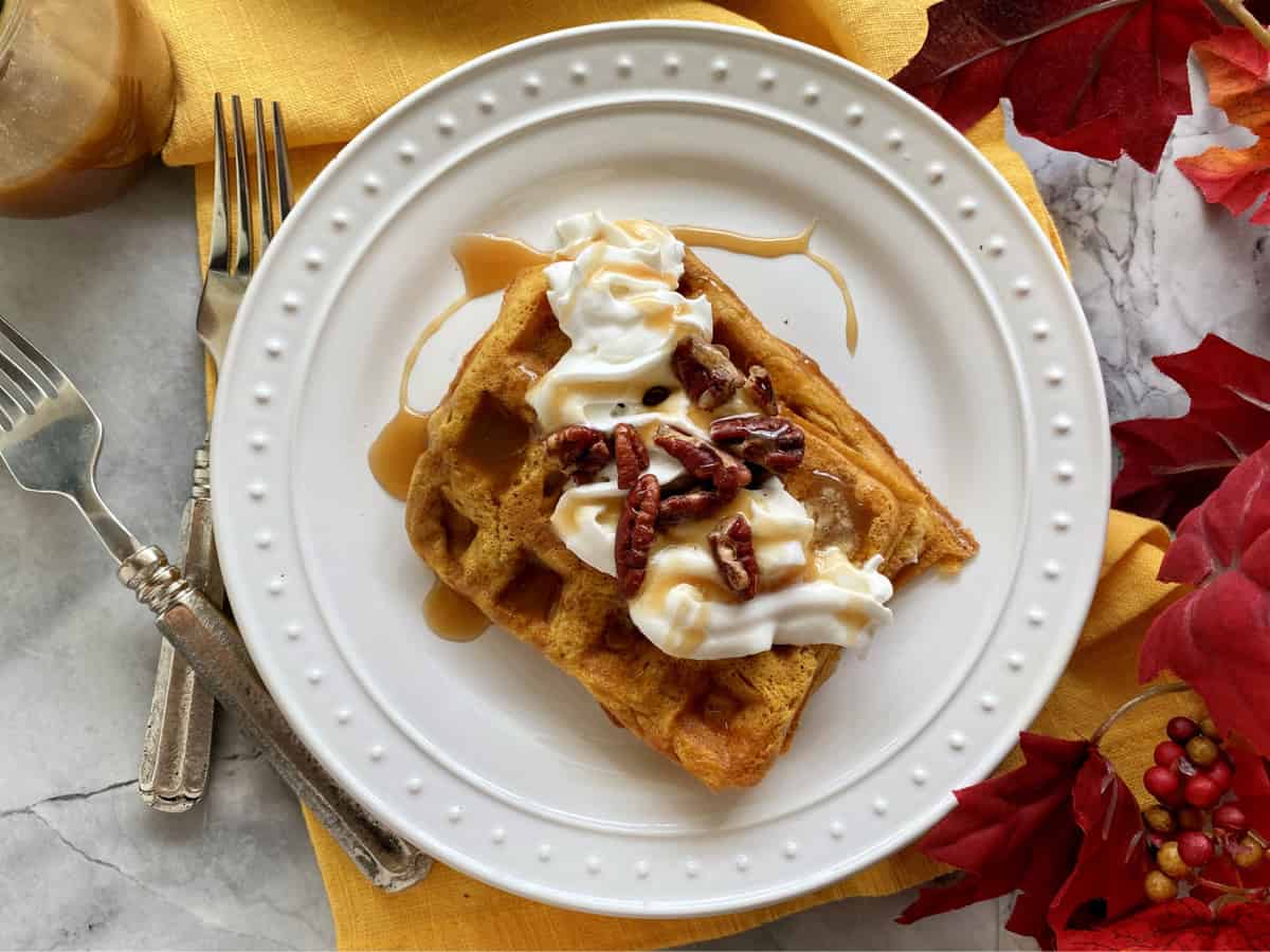 Top view of a white plate with two rectangular waffles with whipped cream and pecans.