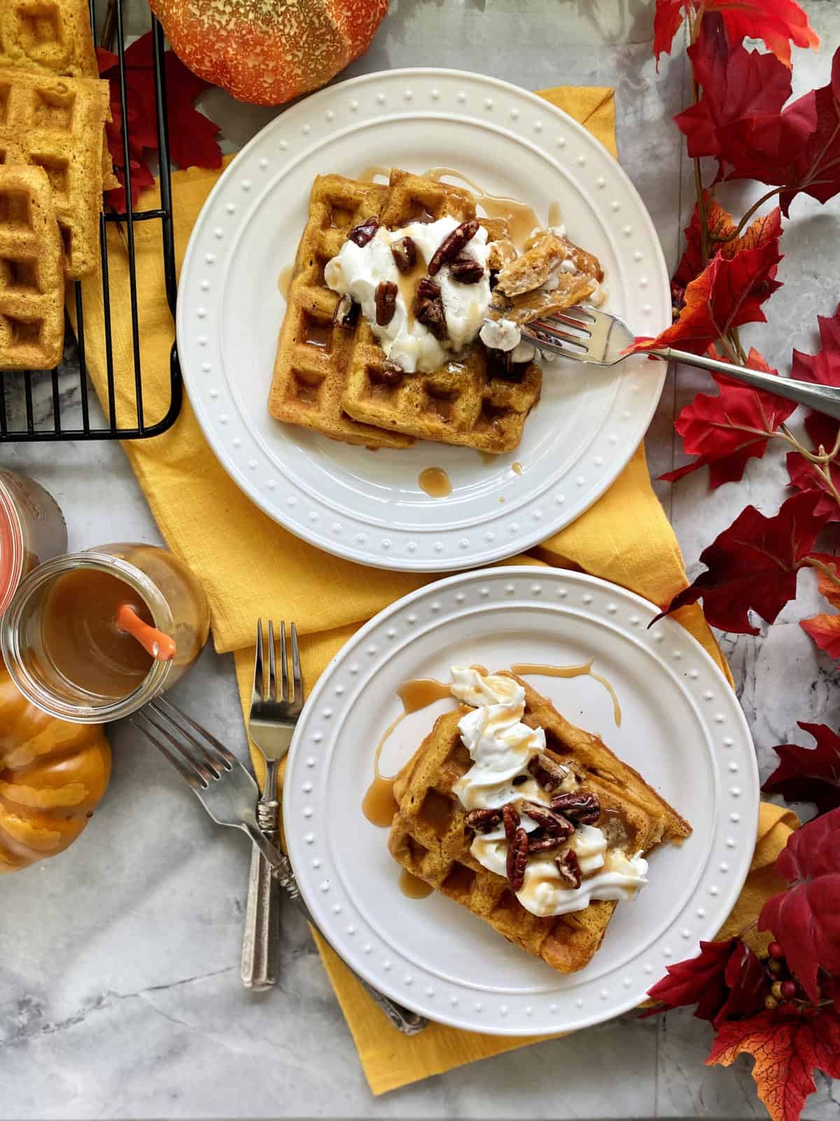 Top view of two white plates with waffles stacked topped with whipped cream.