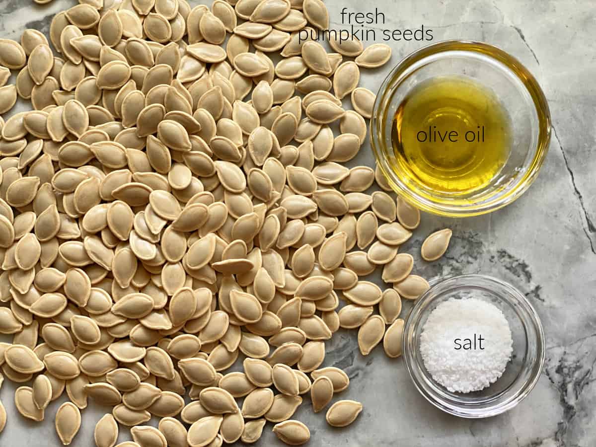 Ingredients laid out on marble countertop: pumpkin seeds, olive oil, salt.