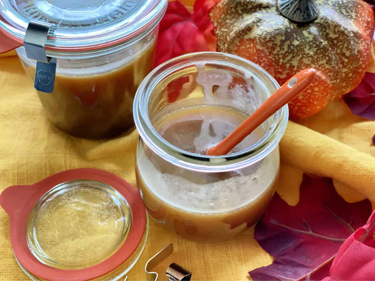 Two glass jars filled with caramel sauce with fall leaves and pumpkins.