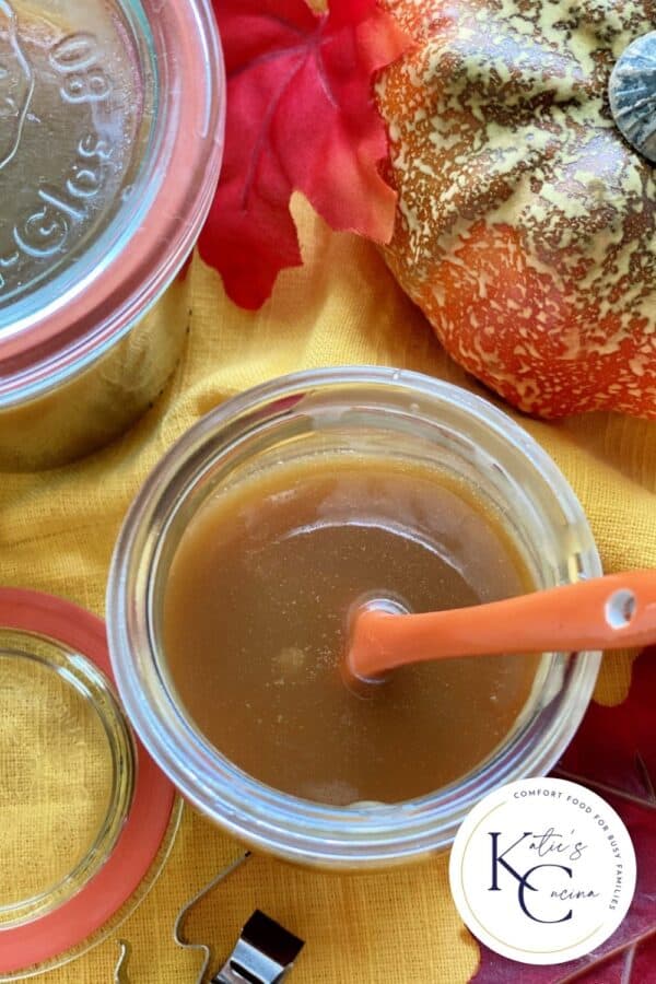 Top view of an open jar of caramel sauce with an ornage spoon with text on image for Pinterest.