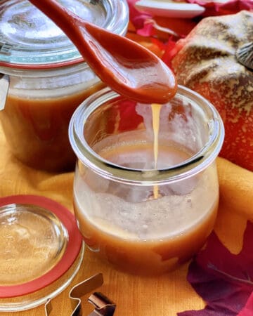 Two glass jars filled with caramel sauce with an orange spoon dripping caramel.