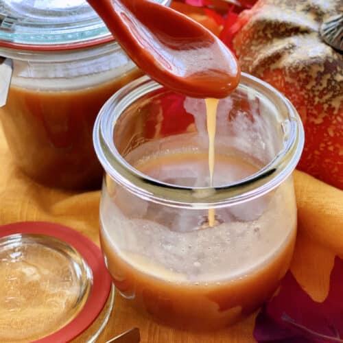 Two glass jars filled with caramel sauce with an orange spoon dripping caramel.