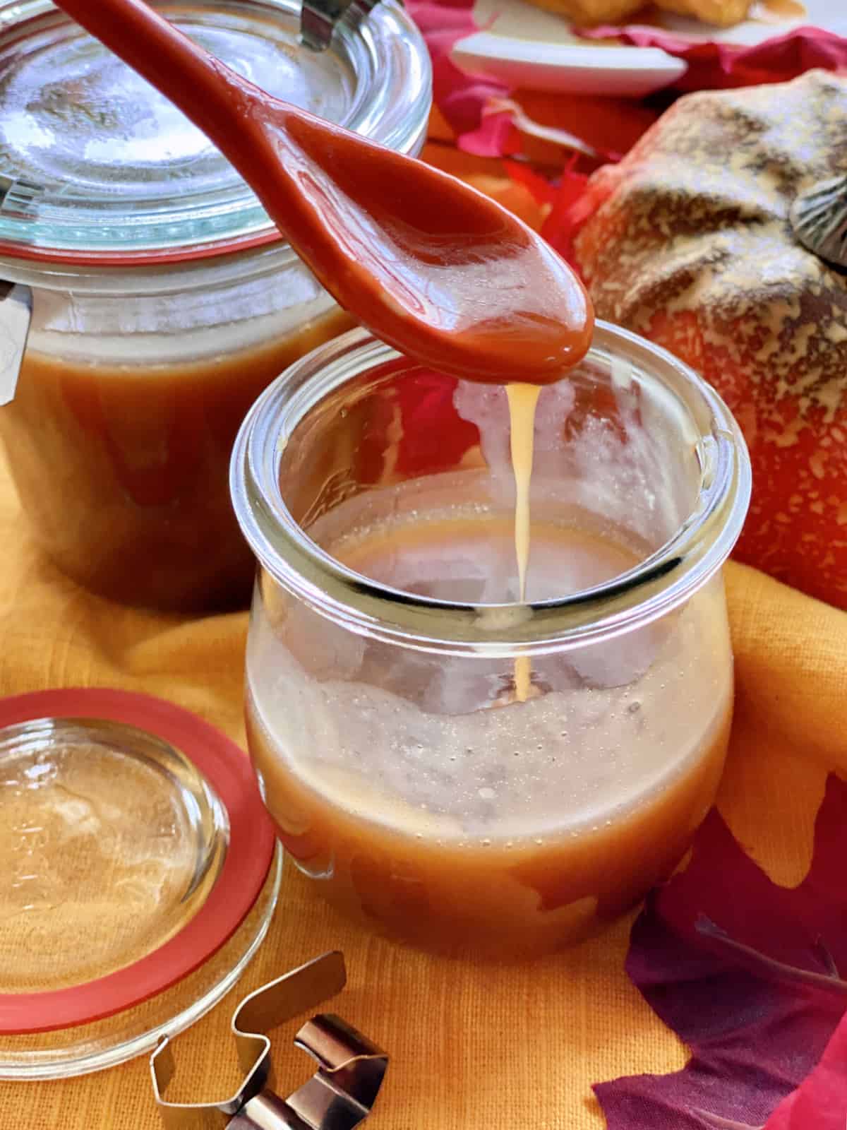 Two glass jars filled with caramel sauce with an orange spoon dripping caramel.