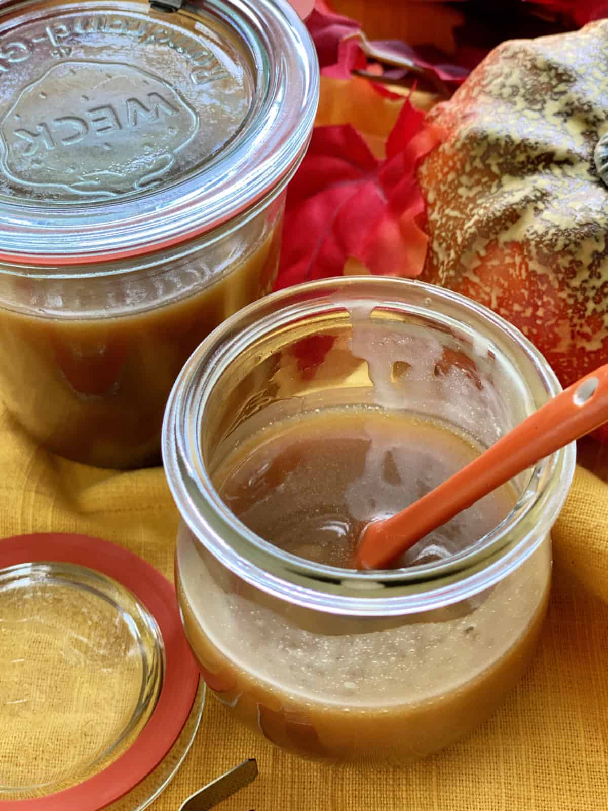 Two glass jars filled with caramel on a yellow cloth with fall leaves.