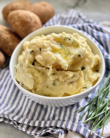 Mashed potatoes in a white bowl sitting on a blue and white towel.