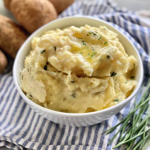 Mashed potatoes in a white bowl sitting on a blue and white towel.