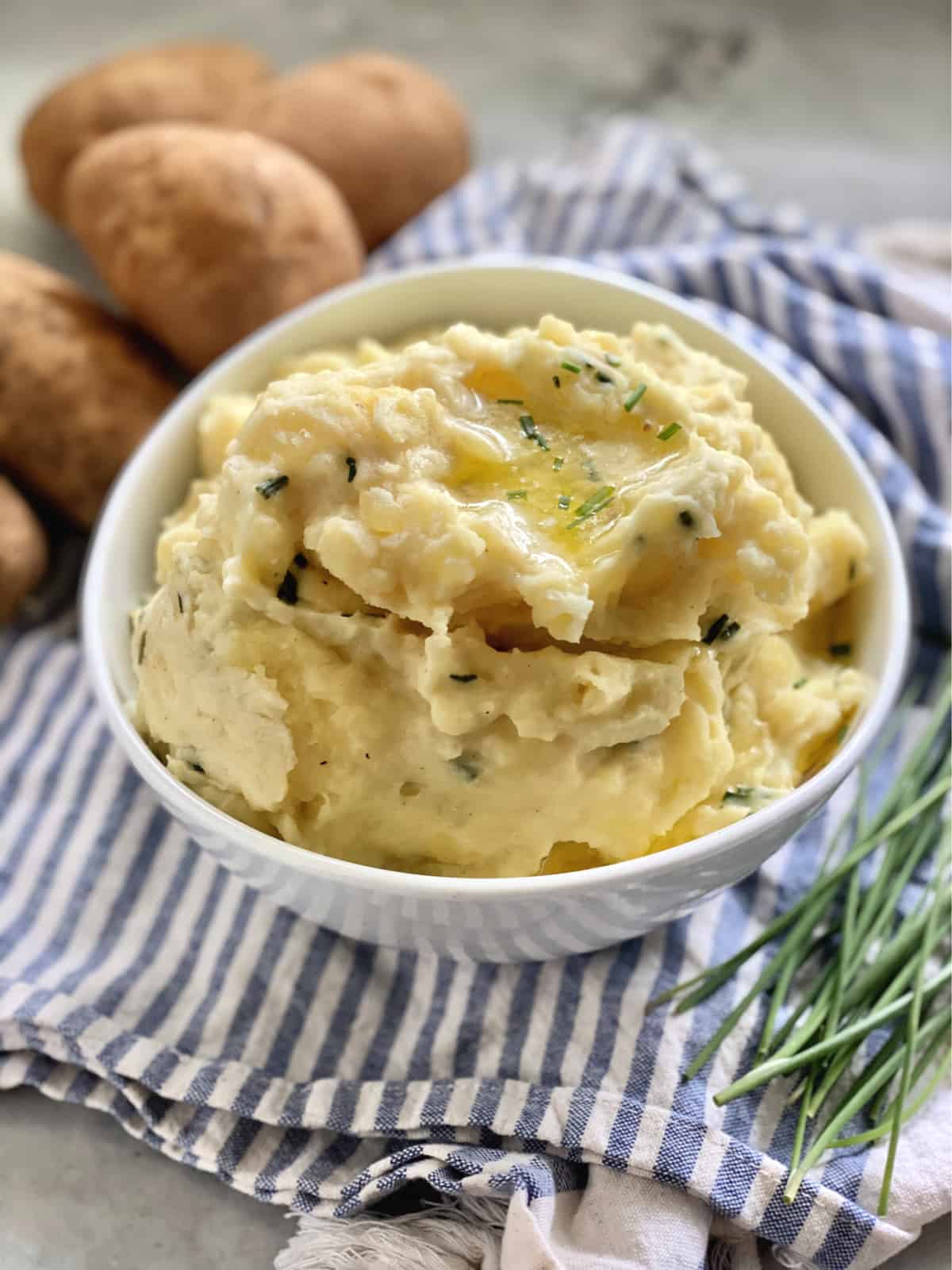 Mashed potatoes in a white bowl sitting on a blue and white towel.