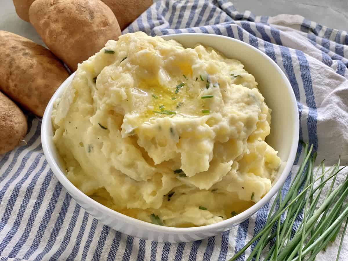 A white bowl filled with mashed potatoes and chives.