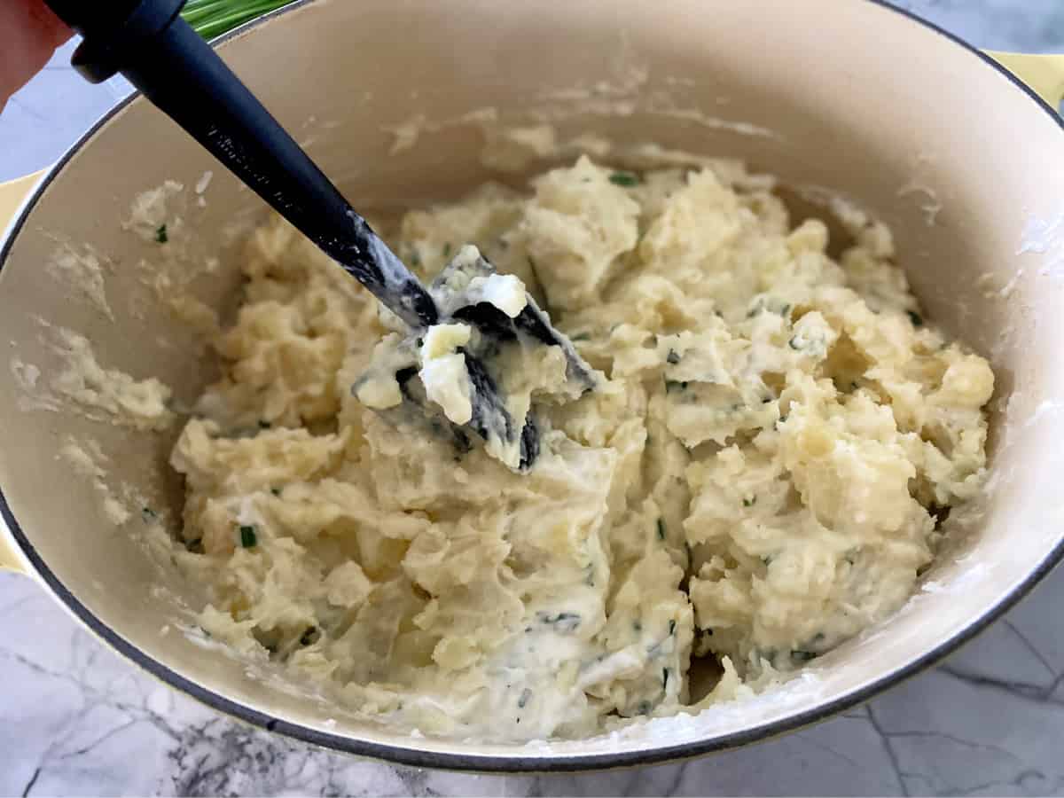 Potatoes mashed in a pot with a black potato masher.