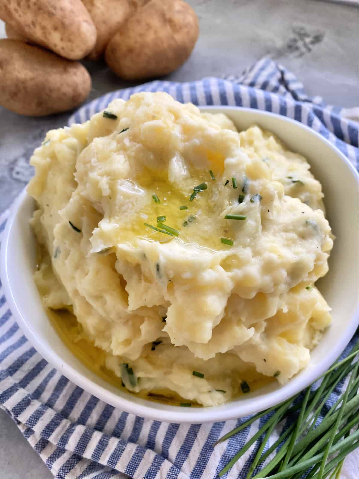 White bowl filled with mashed potatoes, melted butter, and chives.